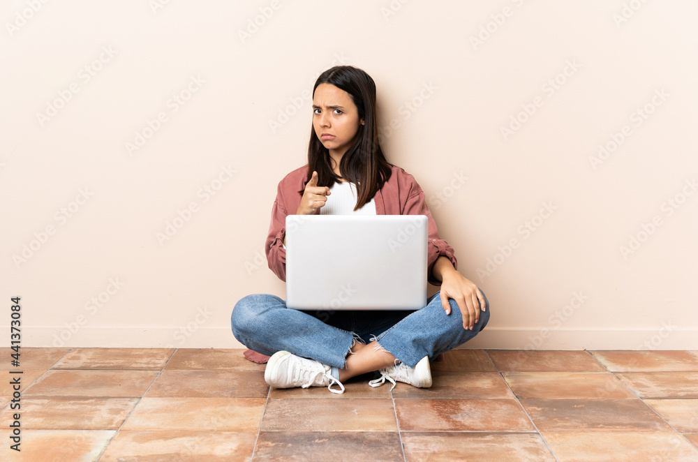 Young mixed race woman with a laptop sitting on the floor frustrated and pointing to the front Young mixed race woman with a laptop sitting on the floor frustrated and pointing to the front