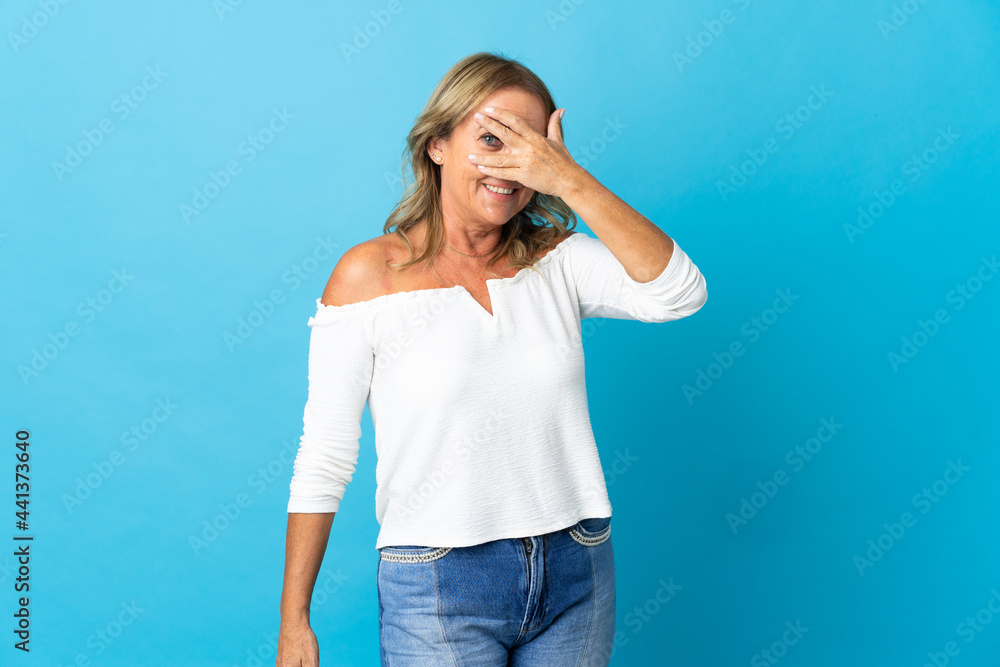 Middle aged blonde woman over isolated background covering eyes by hands and smiling Middle aged blonde woman over isolated background covering eyes by hands and smiling