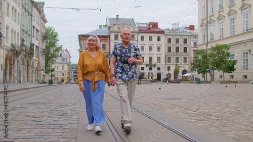 Senior old stylish tourists man and woman having a walk and talking in city Lviv, Ukraine. Elderly grandmother, grandfather with photo camera enjoying conversation, traveling together. Mature family
