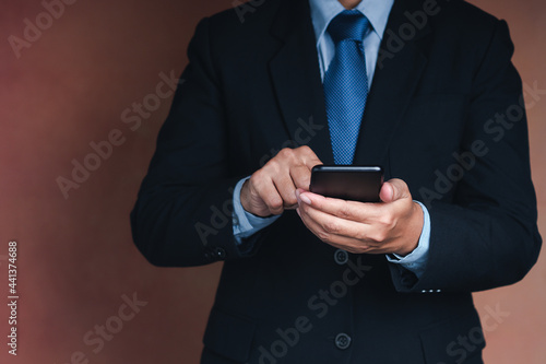 Businessman using a smartphone while standing with a brown background. Space for text. Communication and technology concept