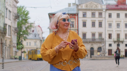 Elderly mature traveler grandmother pensioner getting lost in big city trying to find route. Senior stylish tourist woman looking for way using smartphone in old town Lviv  Ukraine. Summer vacation