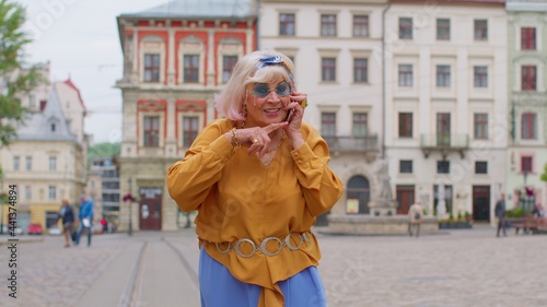 Excited elderly old tourist woman talking on mobile phone while walking on city street of Lviv, Ukraine. Senior stylish mature granny enjoying smartphone conversation and traveling. Urban concept
