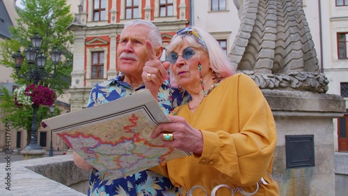 Senior couple grandmother and grandfather tourists in stylish clothing looking for a place to go in new city Lviv, Ukraine, using paper map. Elderly family man, woman on holidays vacation traveling