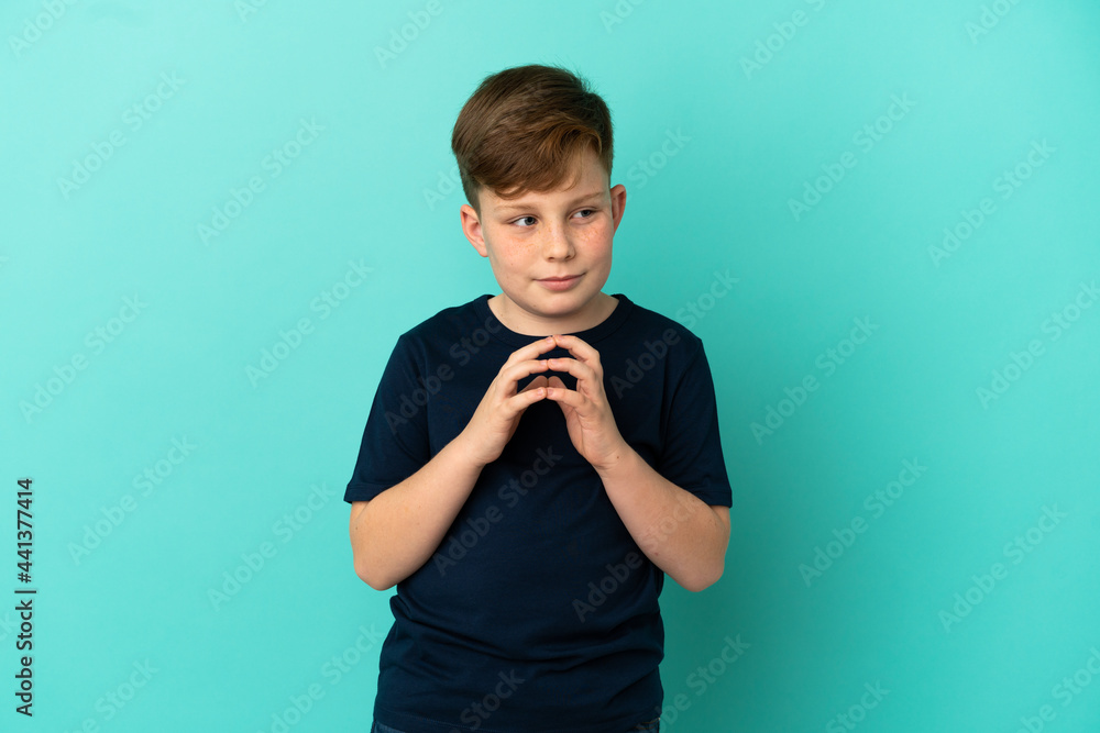 Fototapeta premium Little redhead boy isolated on blue background scheming something