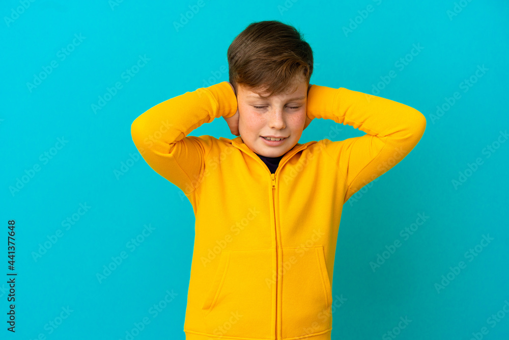 Little redhead boy isolated on blue background frustrated and covering ears Little redhead boy isolated on blue background frustrated and covering ears