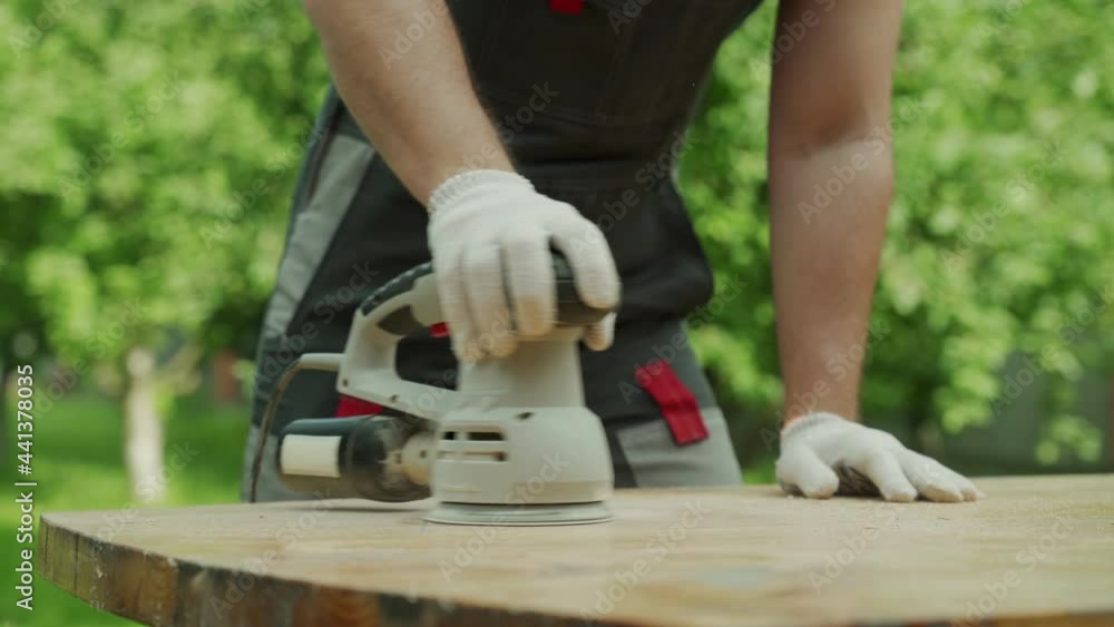 Close-up male carpenter polishes a wooden table with a grinding machine Close-up male carpenter polishes a wooden table with a grinding machine