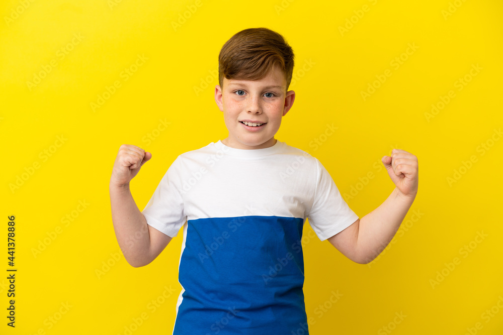 Little redhead boy isolated on yellow background celebrating a victory in winner position Little redhead boy isolated on yellow background celebrating a victory in winner position