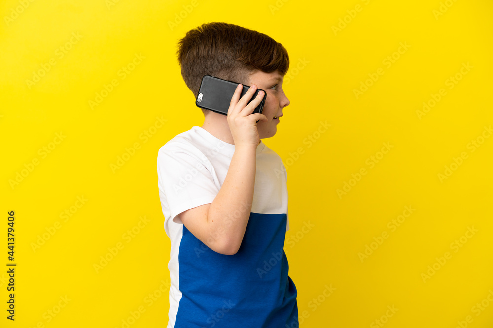 Little redhead boy isolated on yellow background keeping a conversation with the mobile phone Little redhead boy isolated on yellow background keeping a conversation with the mobile phone
