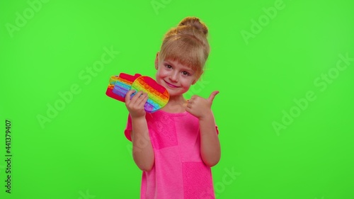 Stylish little child girl holding many colorful squishy silicone bubbles sensory toy. Kid playing push pop it popular educational children game showing thumb up. Advertising, copy-space. Stress relief