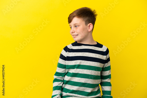Little redhead boy isolated on yellow background looking side