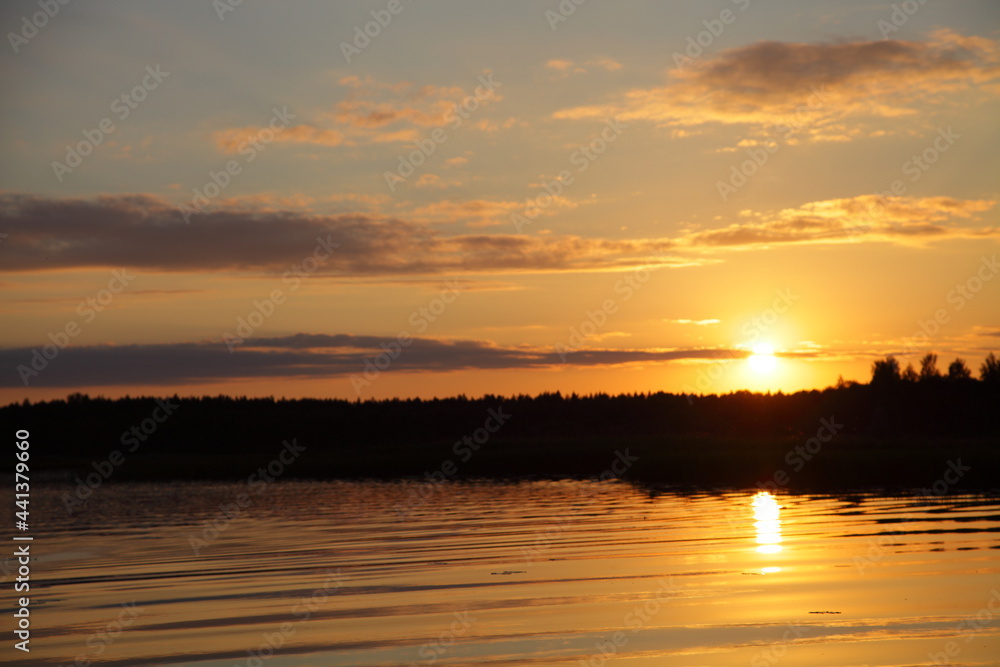 European beautiful orange sunset on the Volga River with a Sun in the sky and a forest on the horizon in the calm water on a summer evening