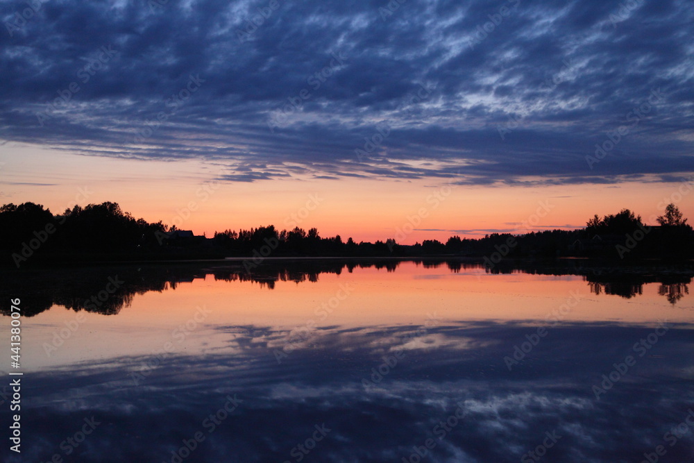 Fototapeta premium A beautiful Russian landscape orange sunset on the Volga River with a reflection of blue clouds in the sky in the calm water and a forest on the horizon on a summer evening