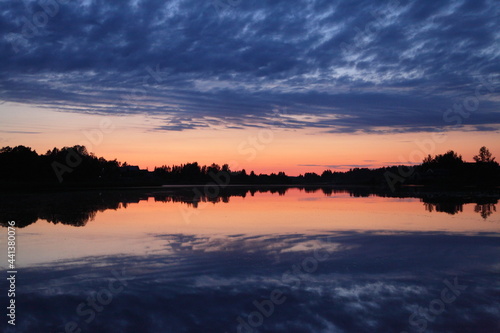 A beautiful Russian landscape orange sunset on the Volga River with a reflection of blue clouds in the sky in the calm water and a forest on the horizon on a summer evening © Ilya