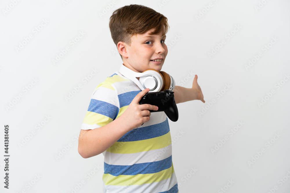 Fototapeta premium Little redhead boy holding a game pad isolated on white background extending hands to the side for inviting to come