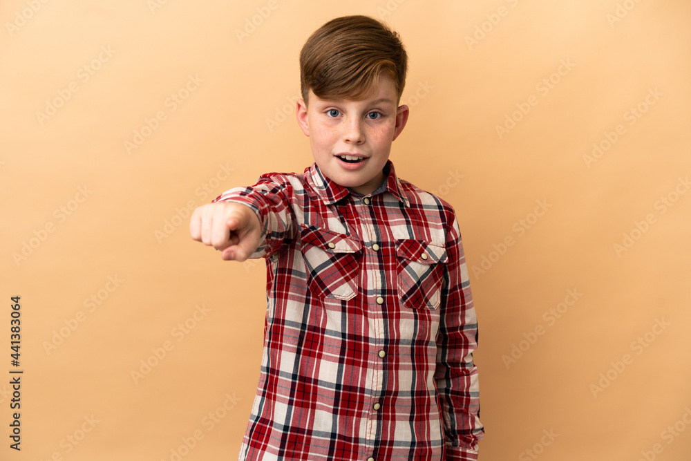 Little redhead boy isolated on beige background surprised and pointing front Little redhead boy isolated on beige background surprised and pointing front