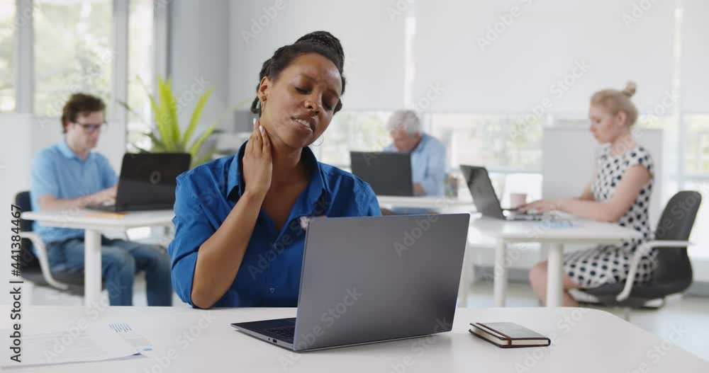 African young woman suffering with pain massaging neck while working in office African young woman suffering with pain massaging neck while working in office