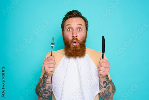 Shocked man with tattoos is ready to eat something with cutlery in hand photo