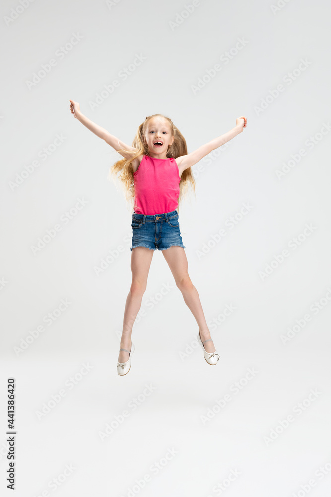 Beautiful little girl in casual clothes jumping isolated on white studio background. Happy childhood concept.