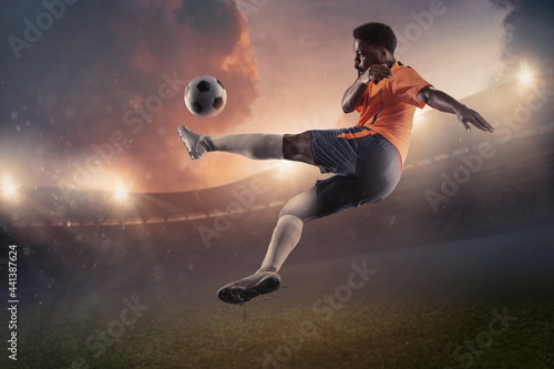 Male soccer, football player kicking ball in jump at the stadium during sport match on dark sky background