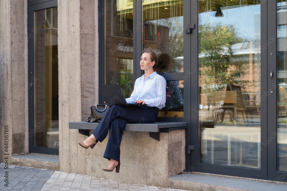 Portrait of business young woman, smiling while sitting on bench outdoors with laptop