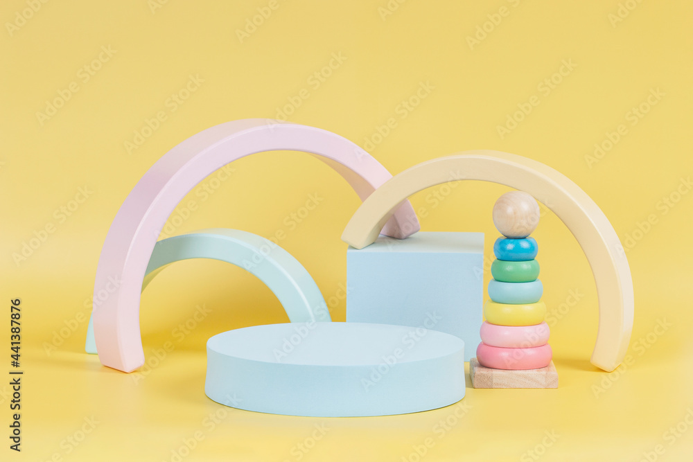 Baby kid toy background. Composition of colorful educational natural wooden toys and geometric shapes podium, platform on pastel yellow background Baby kid toy background. Composition of colorful educational natural wooden toys and geometric shapes podium, platform on pastel yellow background