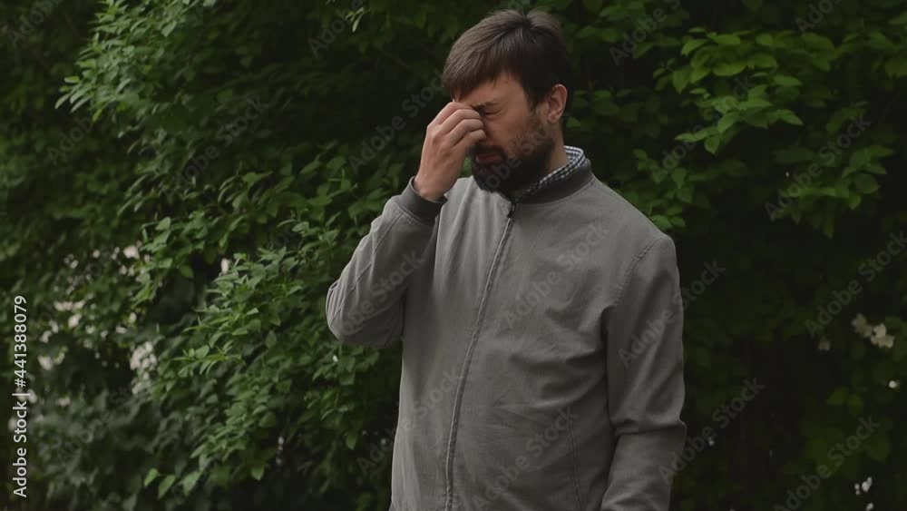 Close up calm tired young bearded man wearing a white shirt takes off his glasses and touches his bridge of nose Close up calm tired young bearded man wearing a white shirt takes off his glasses and touches his bridge of nose