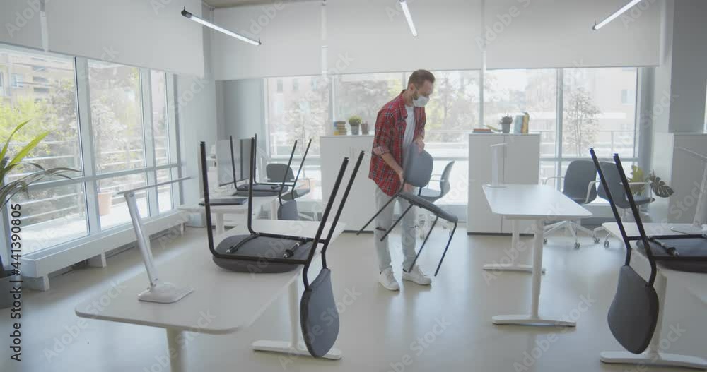 Young man in safety mask putting chairs down in open space office Young man in safety mask putting chairs down in open space office