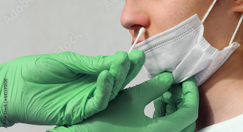 green latex gloves of the doctor performing a nasal swab test for the detection of the Coronavirus virus to the young girl with the mask