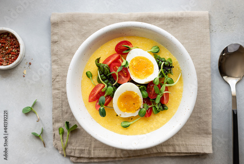 polenta served with fresh vegetables, microgreens and eggs in white bowl on linen napkin. Healthy breakfast or lunch. flat lay