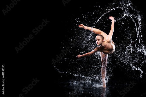 Slender woman in wet sports underwear dancing on surface of water. Ballet dancer is making tricks in liquid splashes. Athletic body is glisten in studio light. Freedom  freshness concept. Modern art.