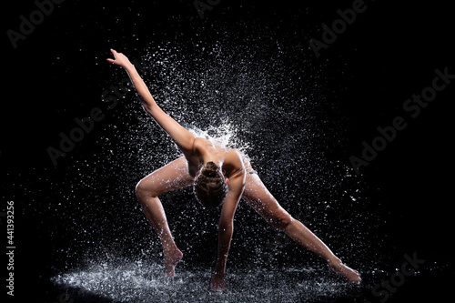 Slender woman in wet sports underwear dancing on surface of water. Ballet dancer is making tricks in liquid splashes. Athletic body is glisten in studio light. Freedom, freshness concept. Modern art.