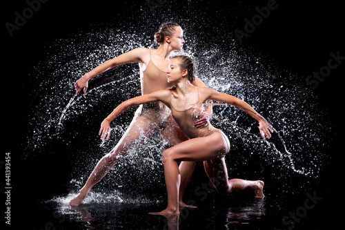 Couple of athletic women are doing dancing tricks under streams, splashes, drops of rain water. Duo acrobats, ballet dancers are performing dance. Freedom and freshness concept. Modern art and beauty.