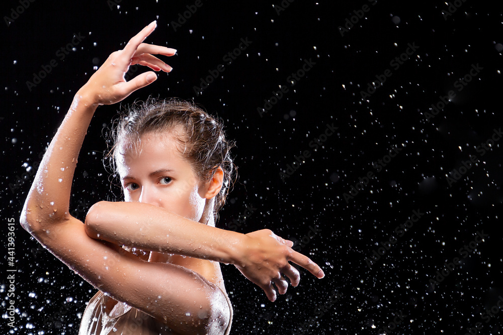 Portrait of sports woman doing stretching under drops of rain. Girl dancer is dancing. Drops of water fall on face against black background. Freedom, freshness concept. Modern art and beauty.