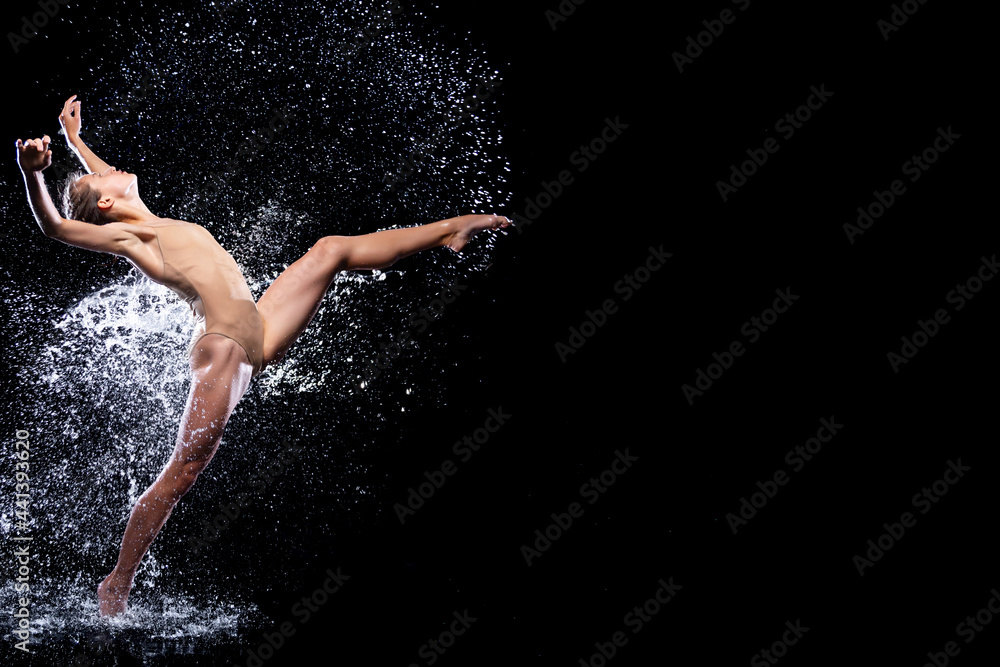 Fototapeta premium Wet young woman in tight beige swimsuit is dancing on floor under rain and splashes, drops of water. Girl modern dancer is doing tricks. Contemporary art dance. Freedom and freshness concept.
