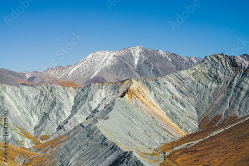 Multicolor autumn landscape with snow-covered mountain and gray rockies with orange and lilac tint. Spectacular colorful view to sharp mountain ridge in fall. Motley mountain scenery in autumn colors.