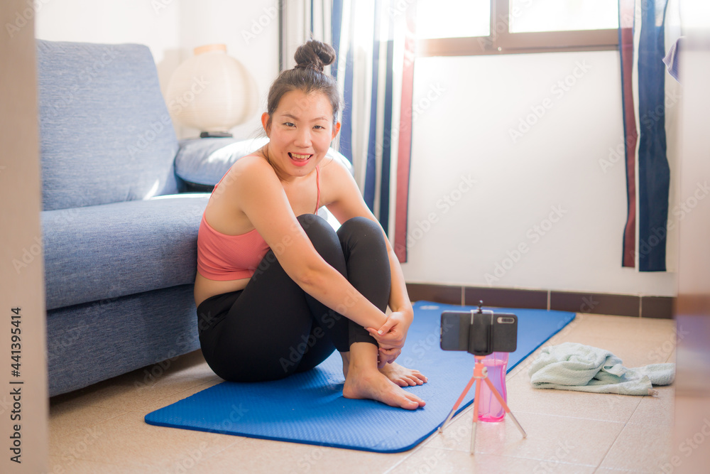 healthy lifestyle portrait of young happy and beautiful Asian Chinese woman smiling sweaty after training workout on yoga mat following online lesson on her phone at home healthy lifestyle portrait of young happy and beautiful Asian Chinese woman smiling sweaty after training workout on yoga mat following online lesson on her phone at home