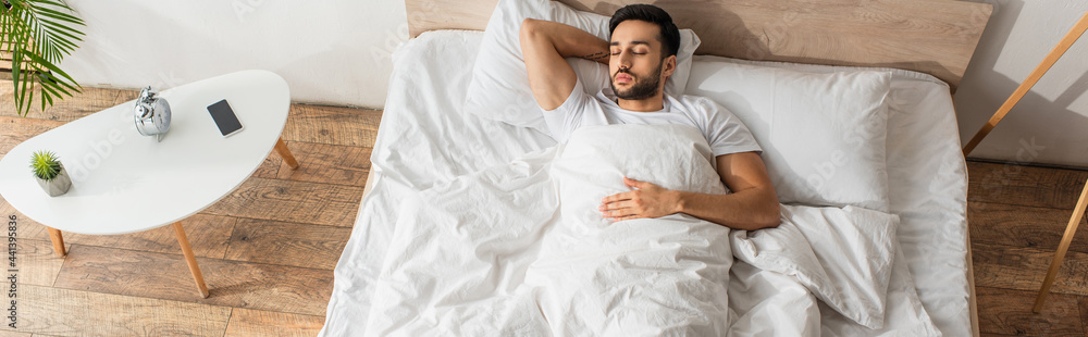 Top view of young man sleeping on bed near alarm clock and mobile phone, banner Top view of young man sleeping on bed near alarm clock and mobile phone, banner