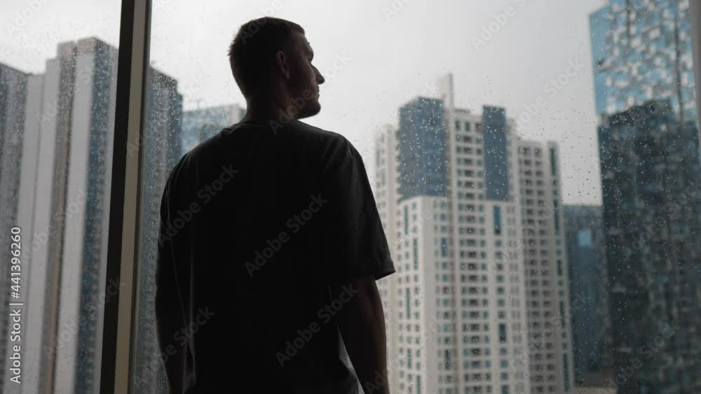 Loneliness in a big city. Back view of a young man looking outside his window on the skyscrapers Loneliness in a big city. Back view of a young man looking outside his window on the skyscrapers