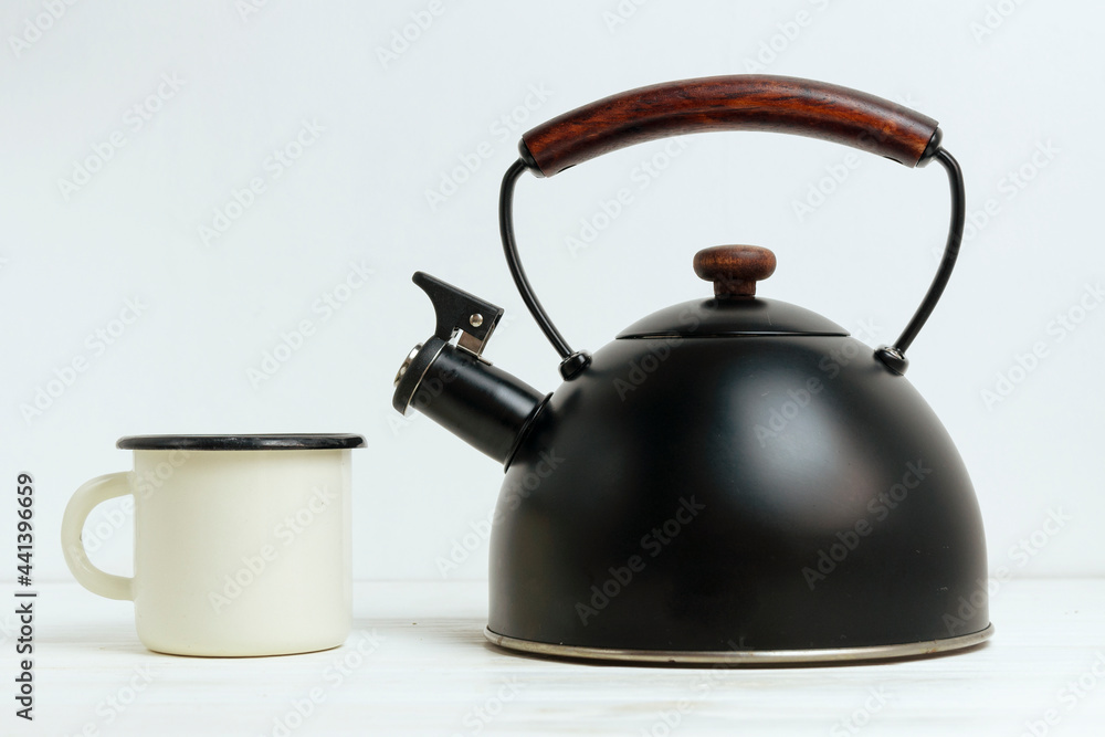 Metal black teapot and enamel mug on a white wooden background. Stylish vintage kitchenware.