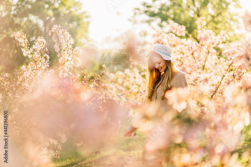 young woman in a hat  with blond hair in a delicate dress  with blooming cherry trees in a spring garden