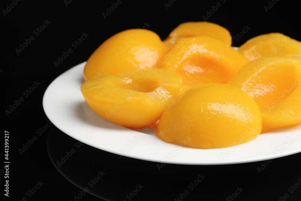 Plate with canned peach halves on black background, closeup