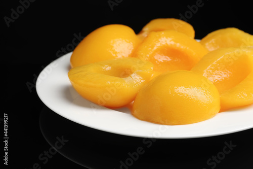 Plate with canned peach halves on black background, closeup