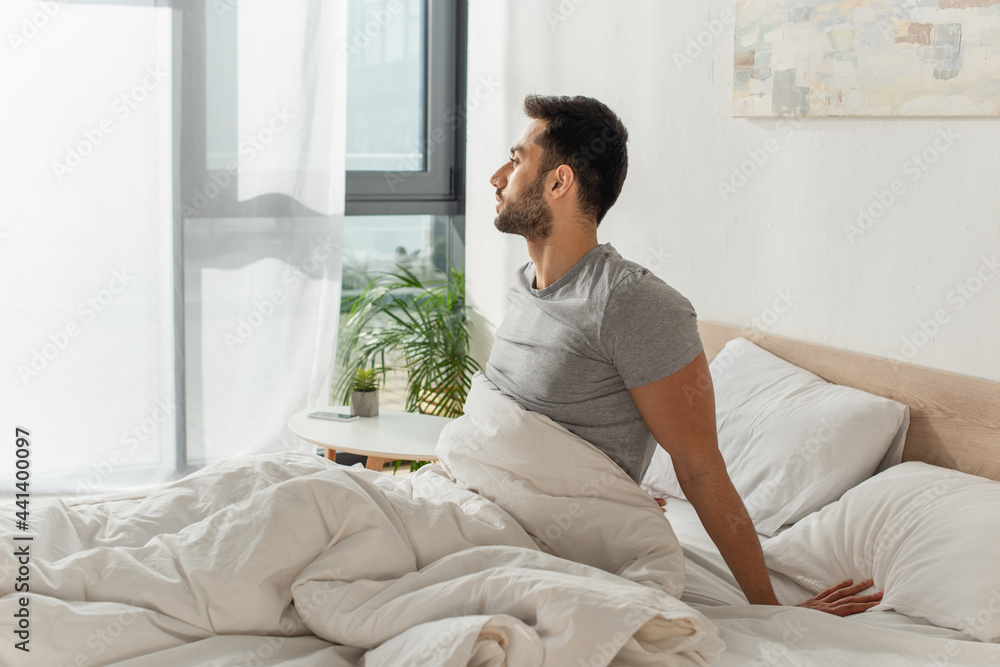 Side view of young bearded man sitting on bed Side view of young bearded man sitting on bed