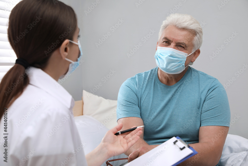 Fototapeta premium Doctor examining senior man with protective mask at nursing home