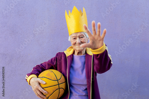 Smiling sportswoman in paper crown with basketball showing stop gesture photo