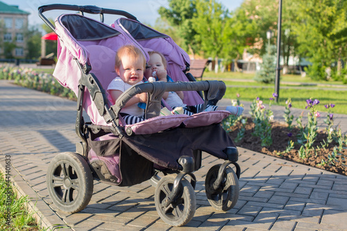 Twins on a walk in a stroller eat fruit puree in city park. © ALEXEY