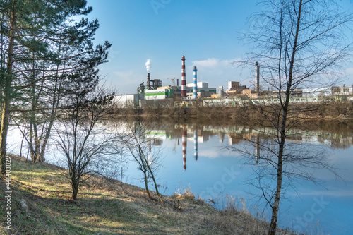 A large factory is located on the river bank. Toxic white smoke escapes from the factory s chimneys. The risk of an environmental disaster. Reflection in the water of the river of the plant