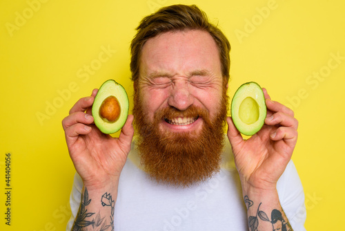 Happy man with beard and tattoos holds an avocado photo