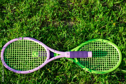 Toy tennis rackets with a ball lying on the grass. Active outdoor games in summer season