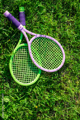 Toy tennis rackets with a ball lying on the grass. Active outdoor games in summer season